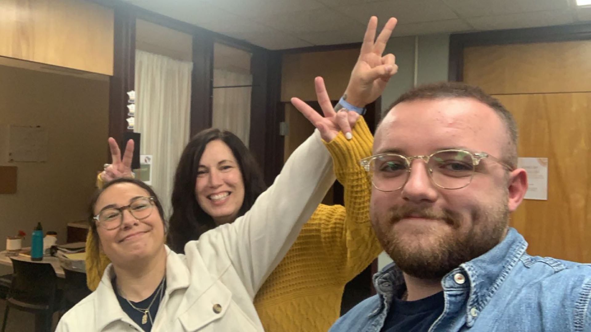 Three people in a candid pose; they are all trying to give each other bunny ears