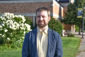 NTC instructor Karl Anderson is wearing a light yellow button-up shirt and a medium-blue jacket. NTC's campus is in the background.