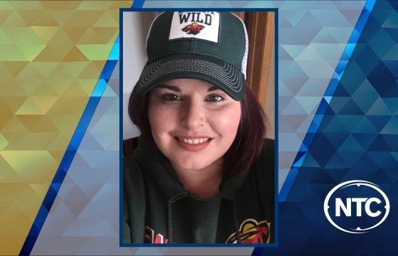 A portrait of a woman with long brown hair wearing a Minnesota Wild jacket and cap.