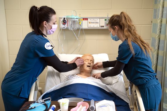 NTC nursing students bent over a lifelike dummy in a hospital bed