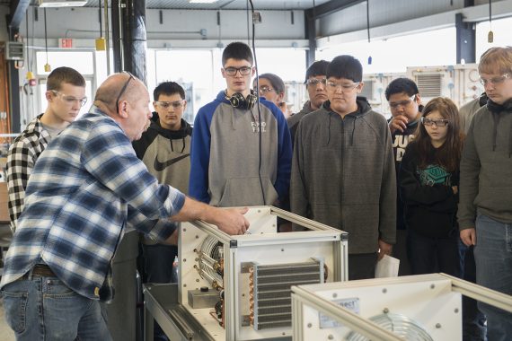 NTC students gathered around a professor holding onto a box with technology inside for an auto building systems class