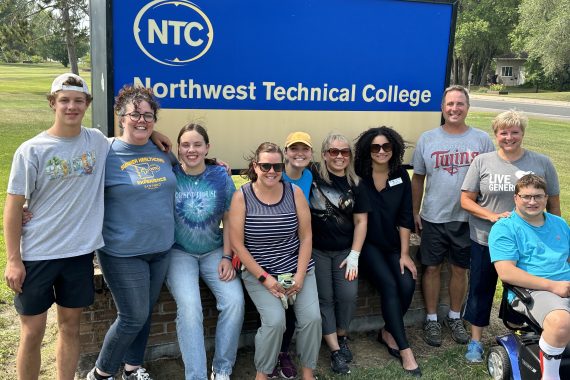 NTC employees and friends pose by the campus sign on the north lawn.
