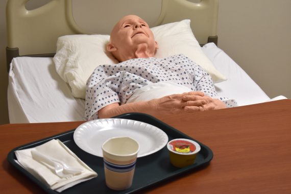 A mannequin of an elderly man a bald head is tucked into a hospital bed in the Sanford/NTC Health Sciences Lab for CNA students at Bemidji High School