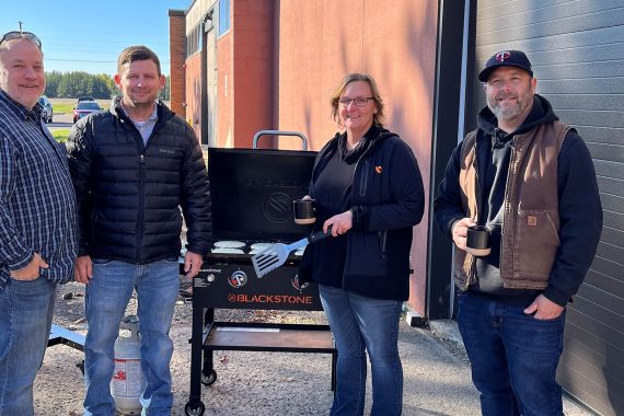 NTC faculty pose by a grill as they prepared lunch for students