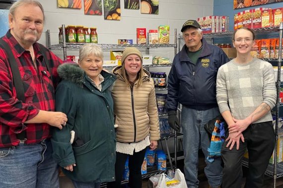 A group of people pose in front of shelves of food.