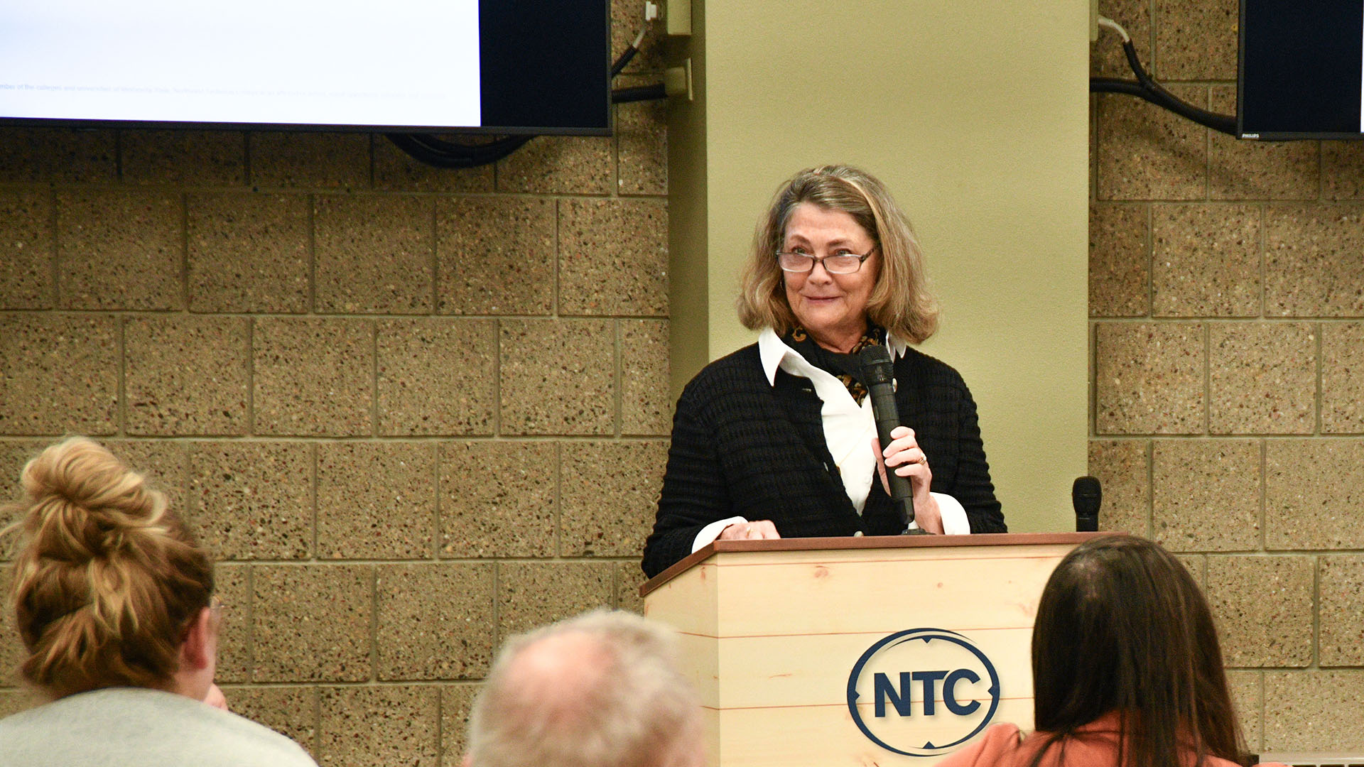 NTC Foundation president Sue Sutton speaks into a microphone behind a lectern with the "NTC" logo on the front