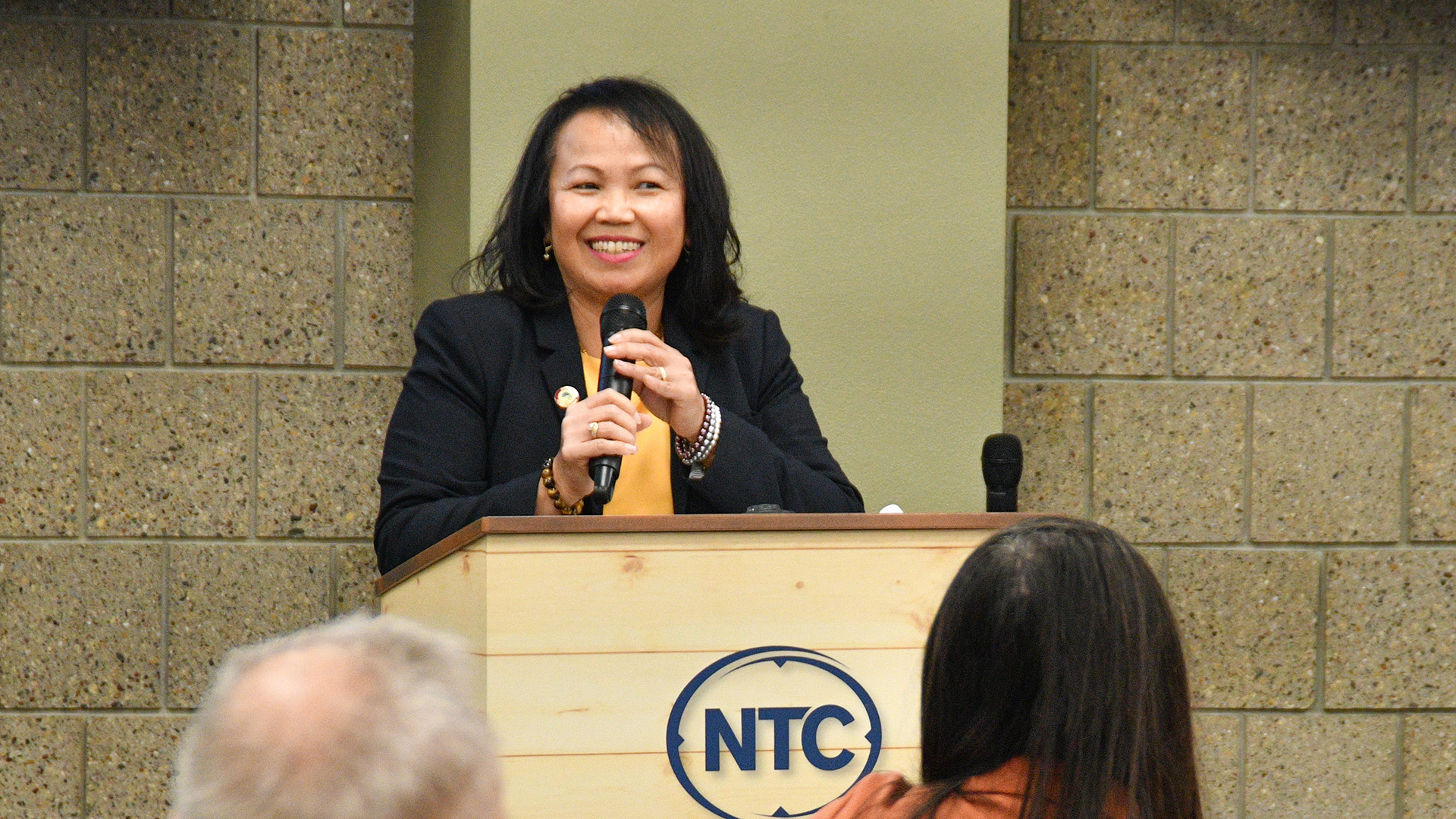 NTC Executive Vice President for Academic Affairs Ketmani Kouanchao speaks into a microphone behind a lectern with an NTC logo on the front.